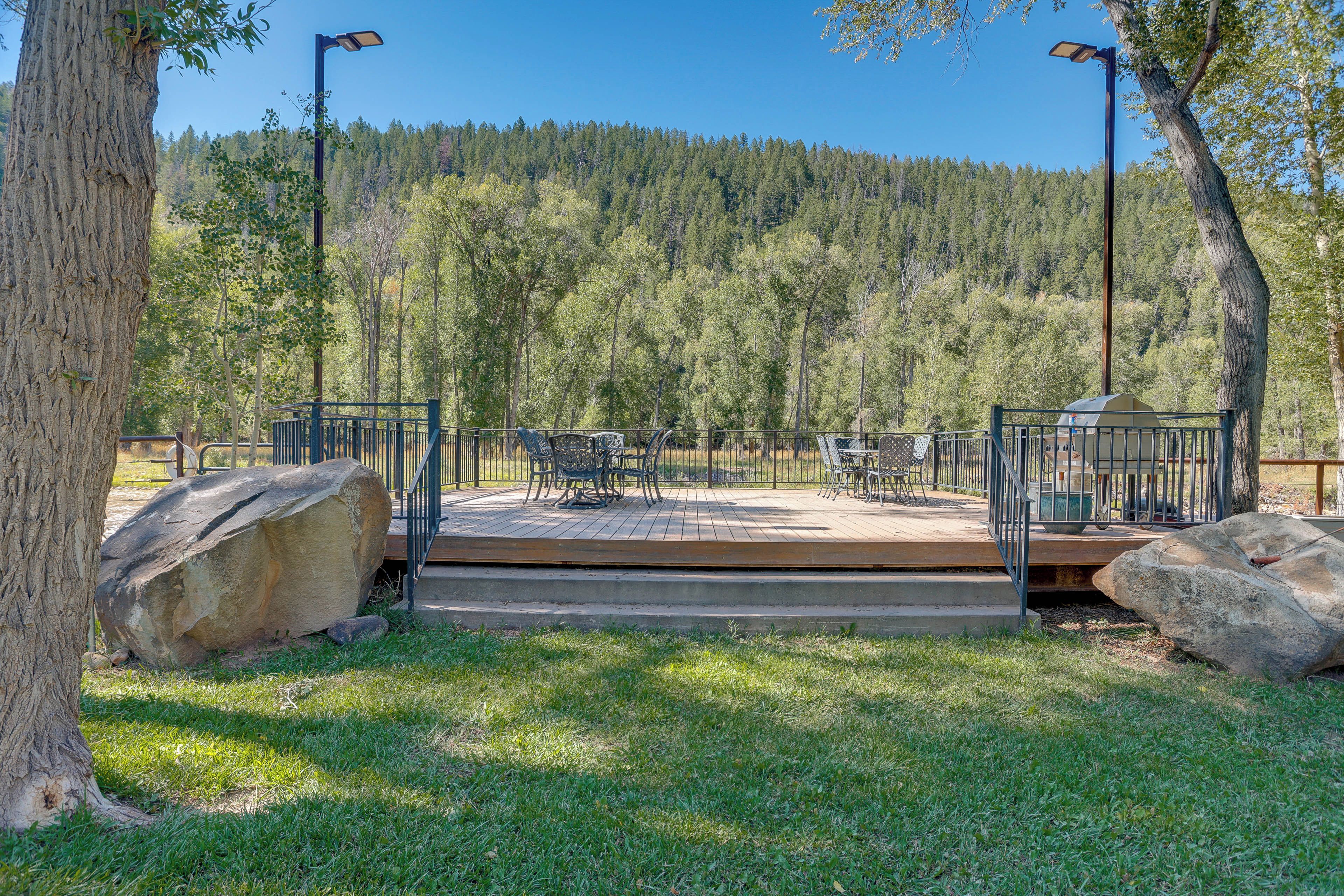 Une terrasse dotée de mobilier d’extérieur, entourée d’une clôture en métal et de gros rochers, et offrant une vue sur une zone boisée.