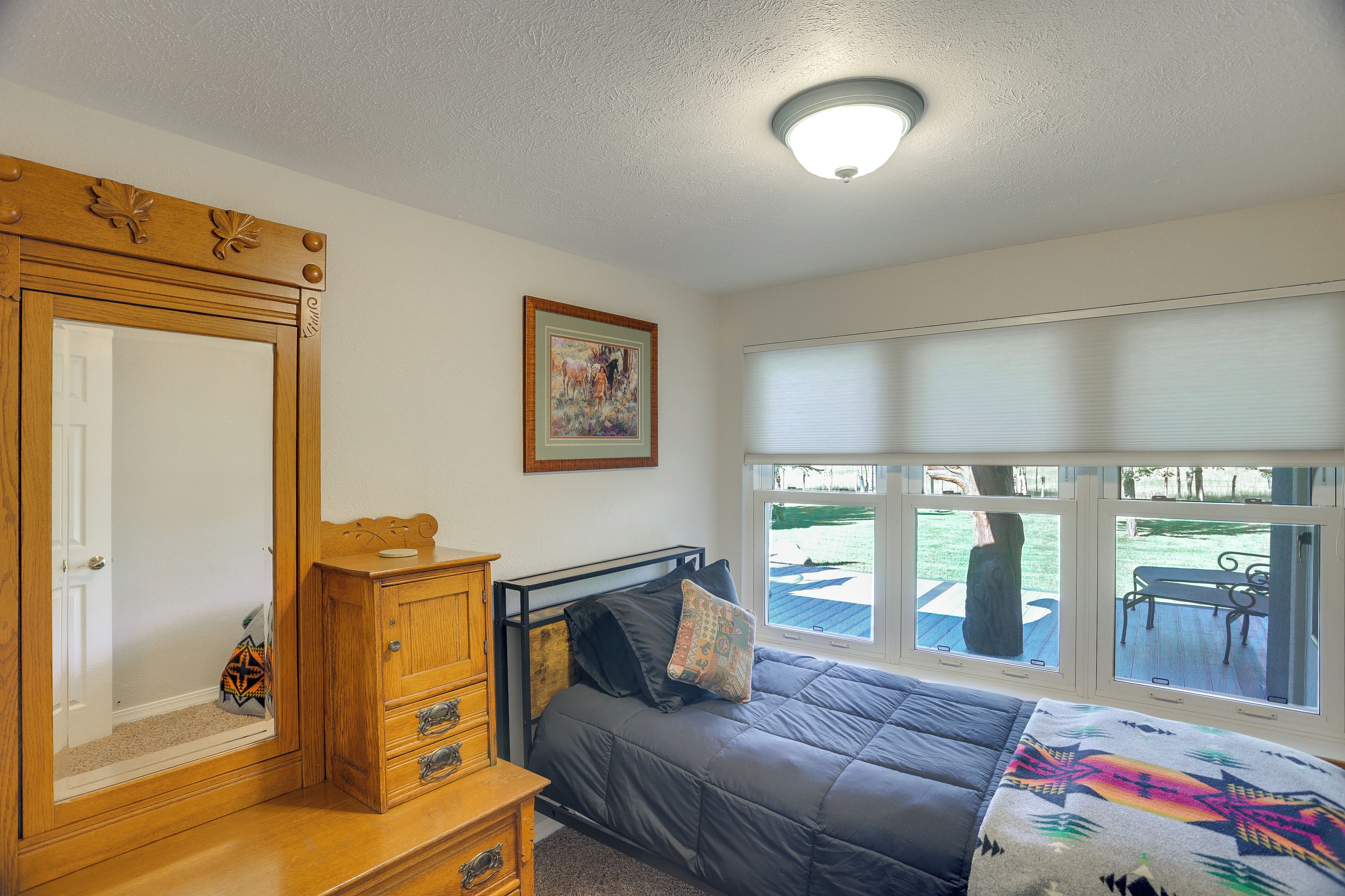 A bedroom with a bed, a dresser, a mirror, a painting, and a window with blinds.