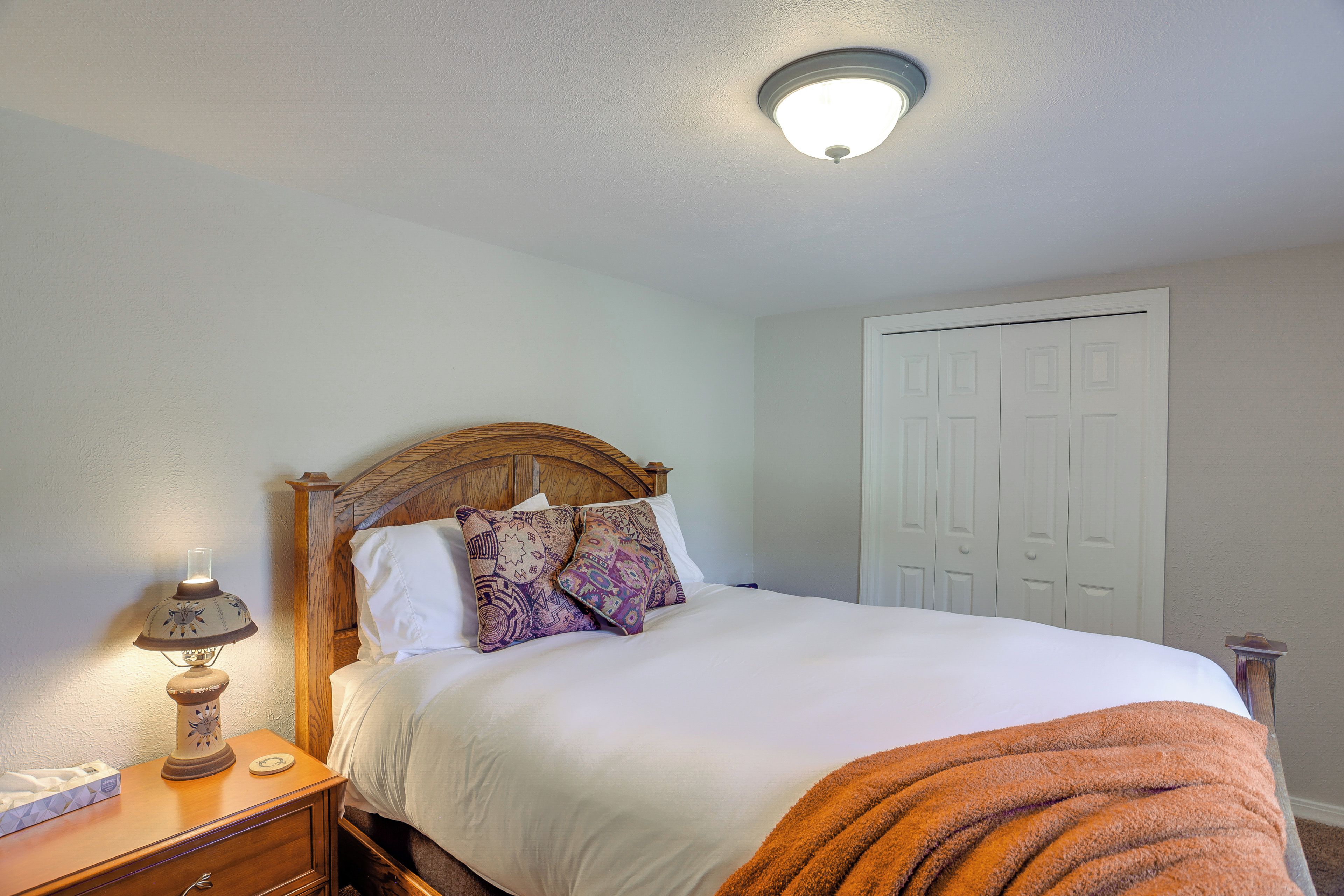 A neatly made bed with a wooden headboard, a bedside lamp, and a door in the background.