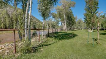 A grassy area with trees and a metal fence, likely part of a park or natural reserve.