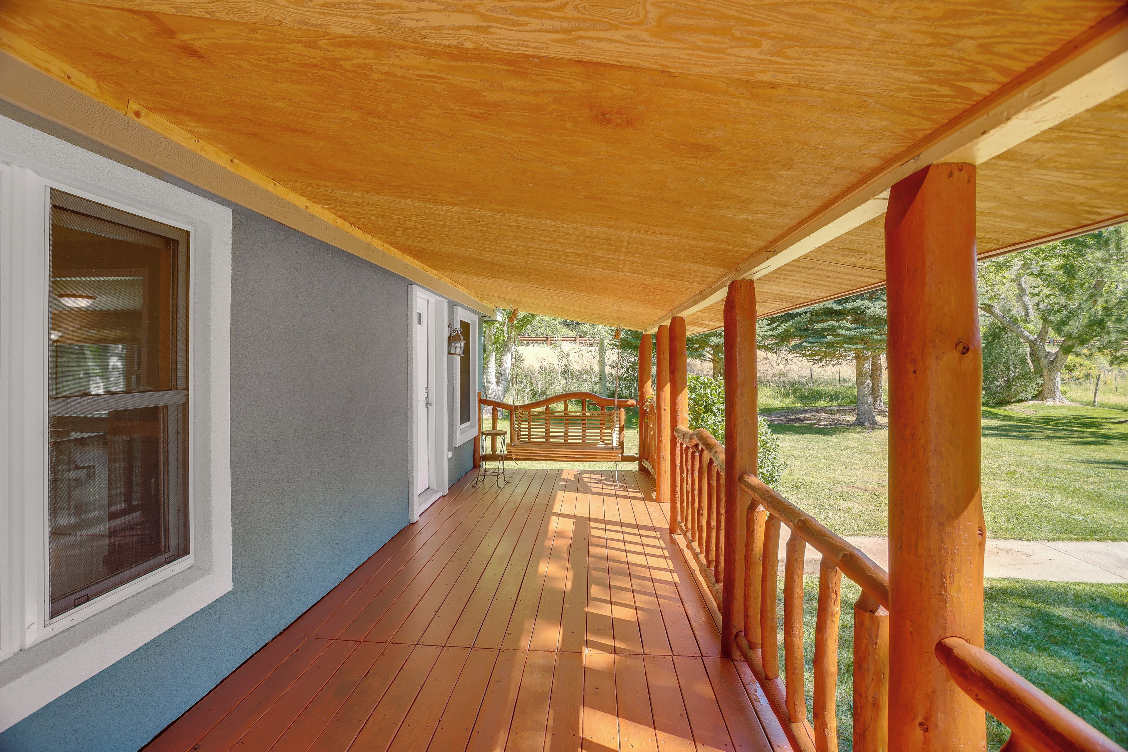A covered wooden deck with a railing, a door, and a window.