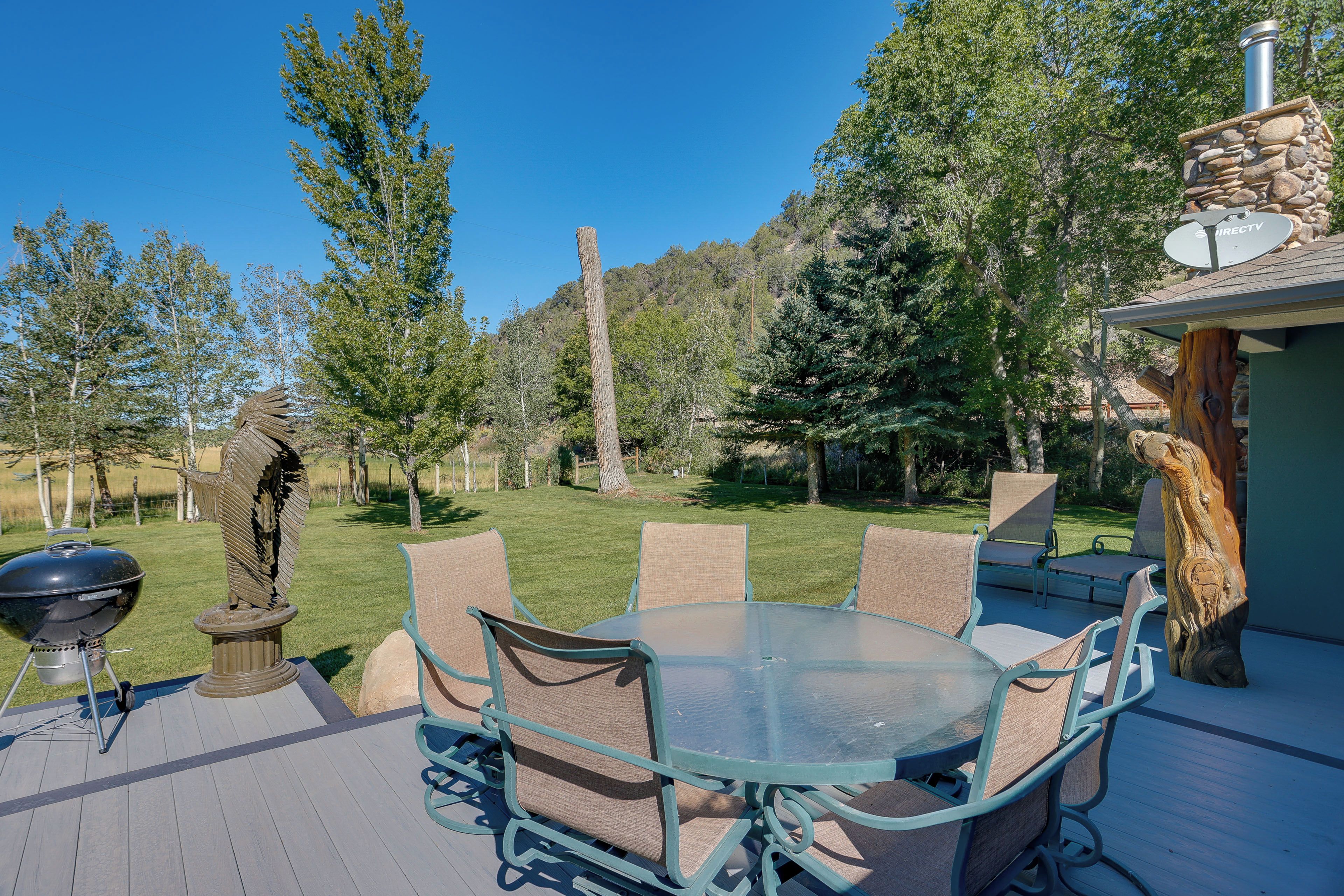 Une terrasse extérieure avec une table et des chaises en verre, un barbecue et une statue.