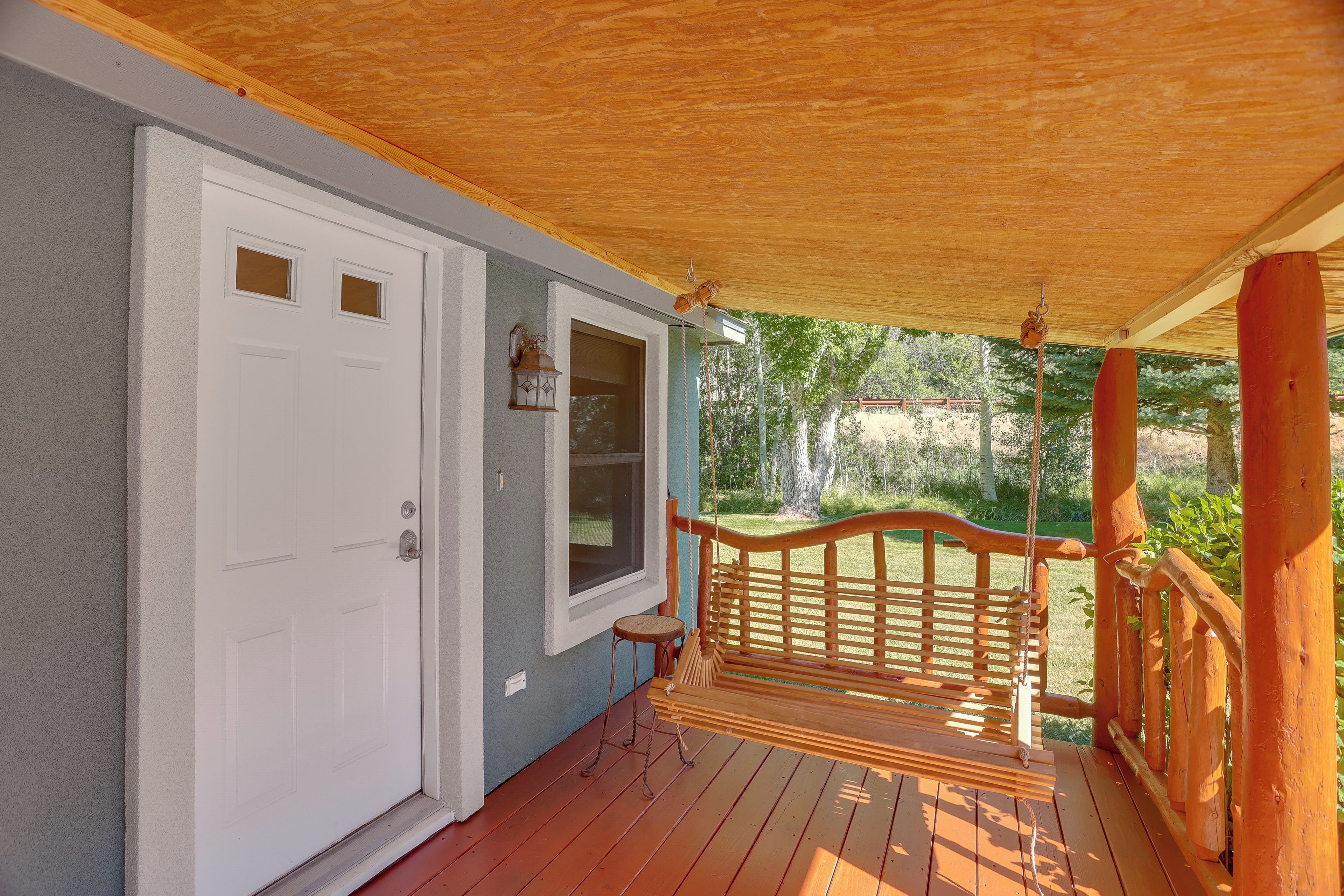 A wooden porch with a swing, a white door, and a window with a view of a garden.