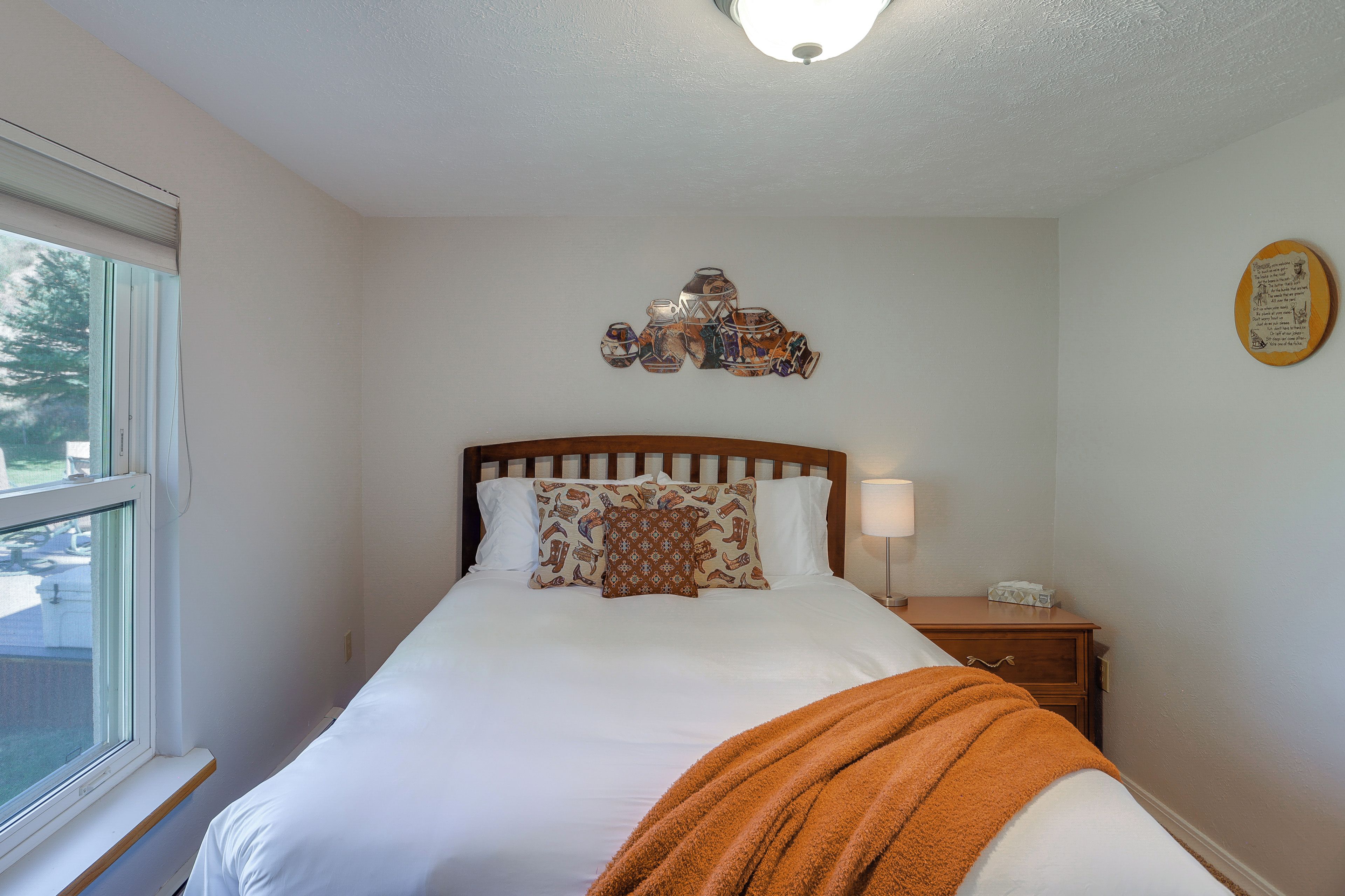 Un dormitorio con cama, mesita de noche, lámpara, ventana y decoración en la pared.