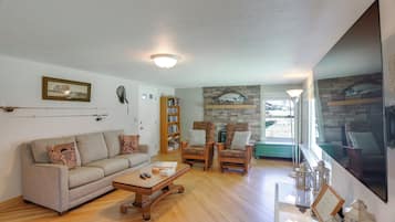 A living room with a sofa, armchairs, a coffee table, a bookshelf, and a stone wall with fish artwork.