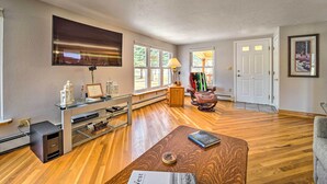 Un salón espacioso con suelo de madera, una mesa de centro de vidrio, un sillón de cuero y un televisor montado en la pared.