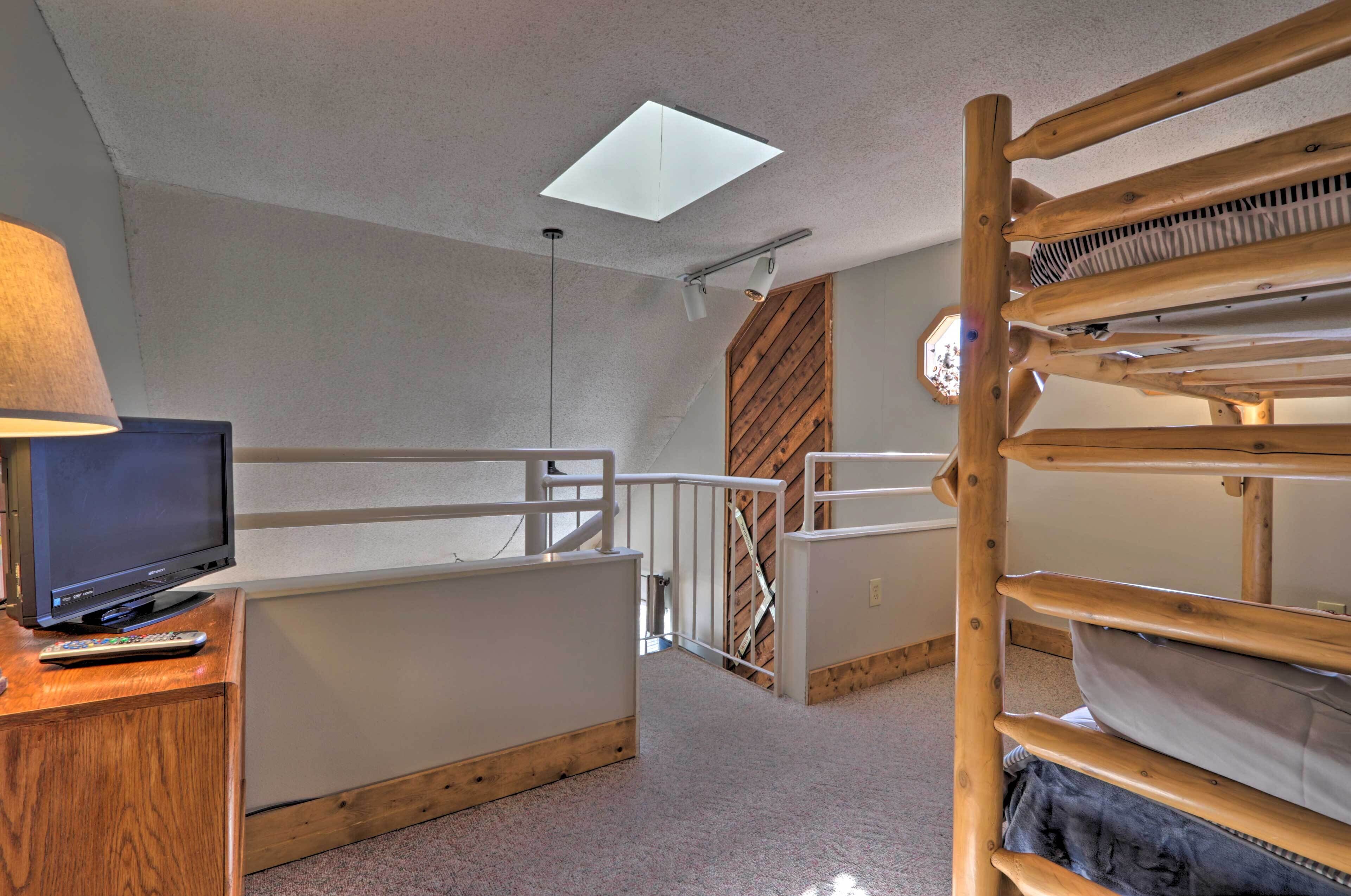 A bedroom with bunk beds, a TV, a lamp, and a skylight.