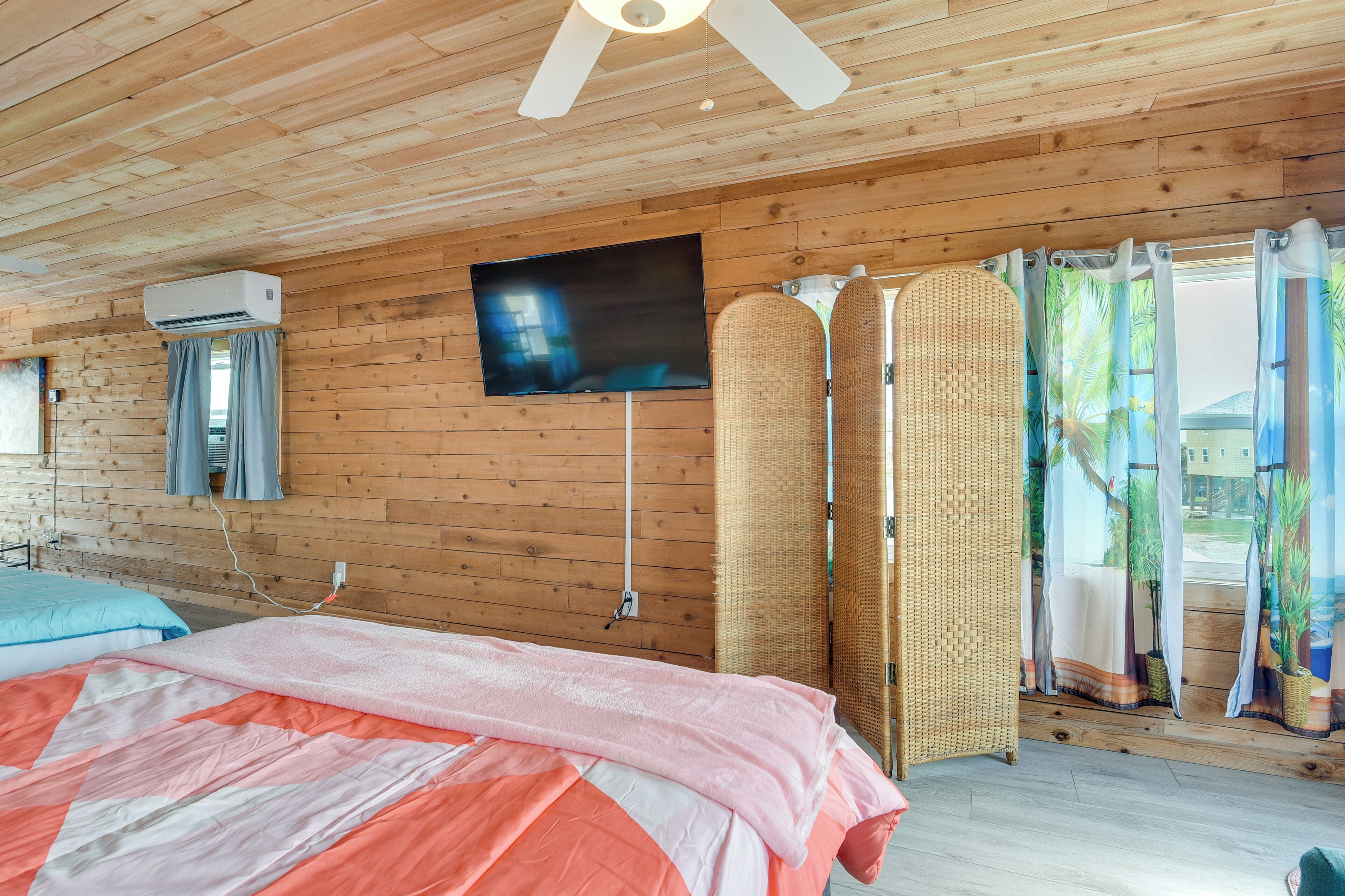 Una habitación con paneles de madera, una cama, un televisor y un ventanal con cortinas.