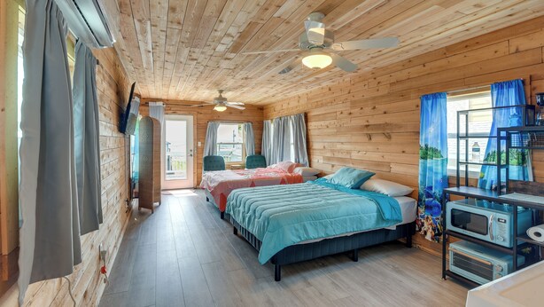 Habitación de cabaña de madera con dos camas, un ventilador de techo, un microondas y una ventana con cortinas.