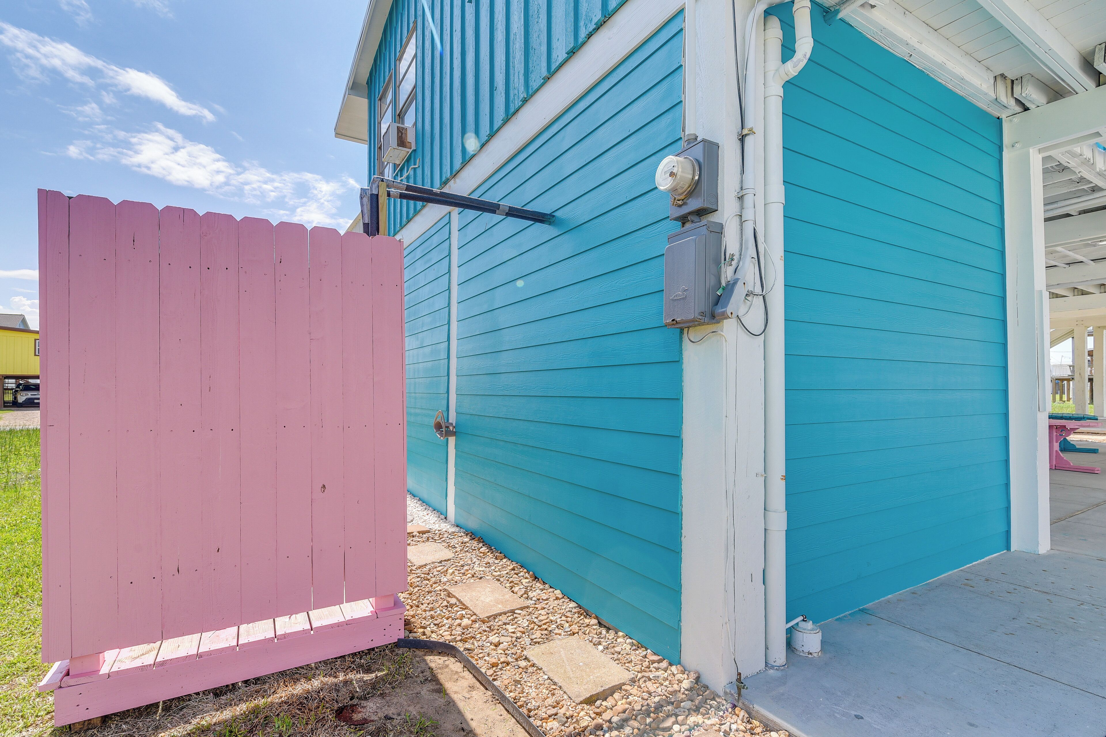 A house with a teal exterior, a pink fence, and a visible garage door.