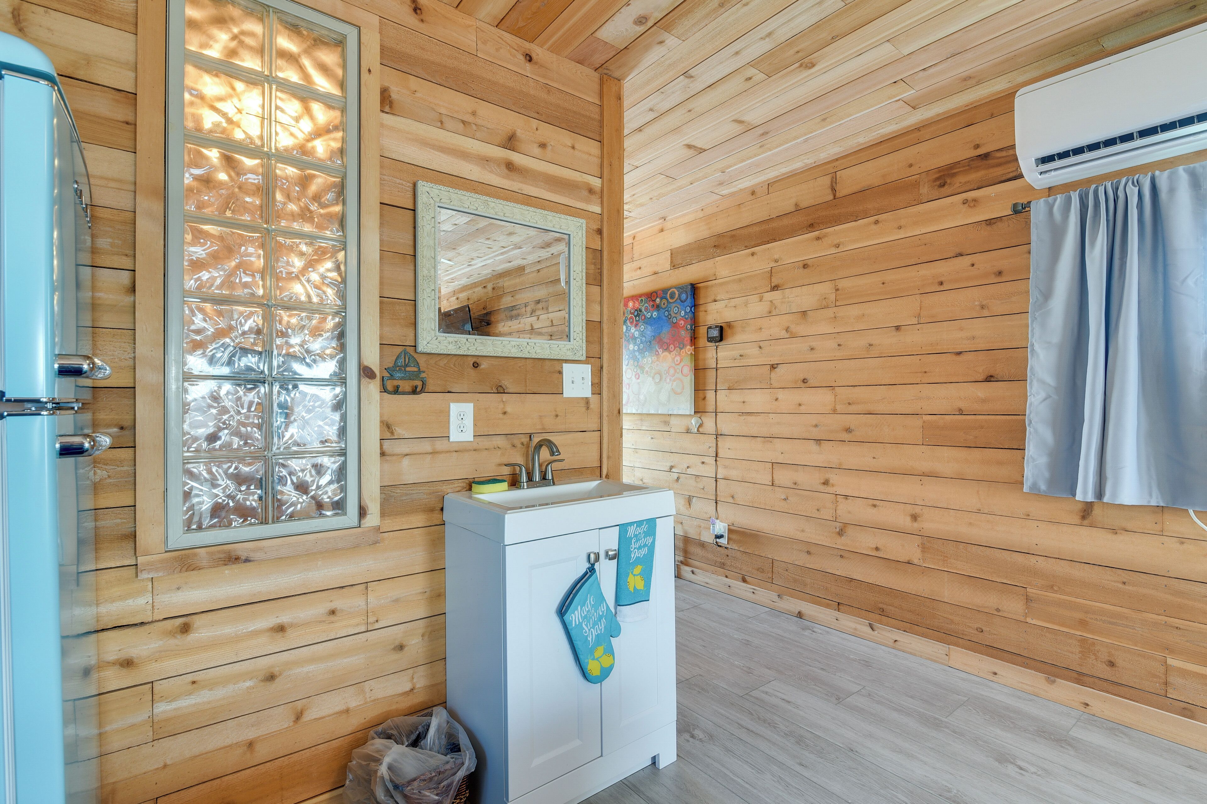 A wooden cabin interior with a white sink, a mirror, and a window with frosted glass.