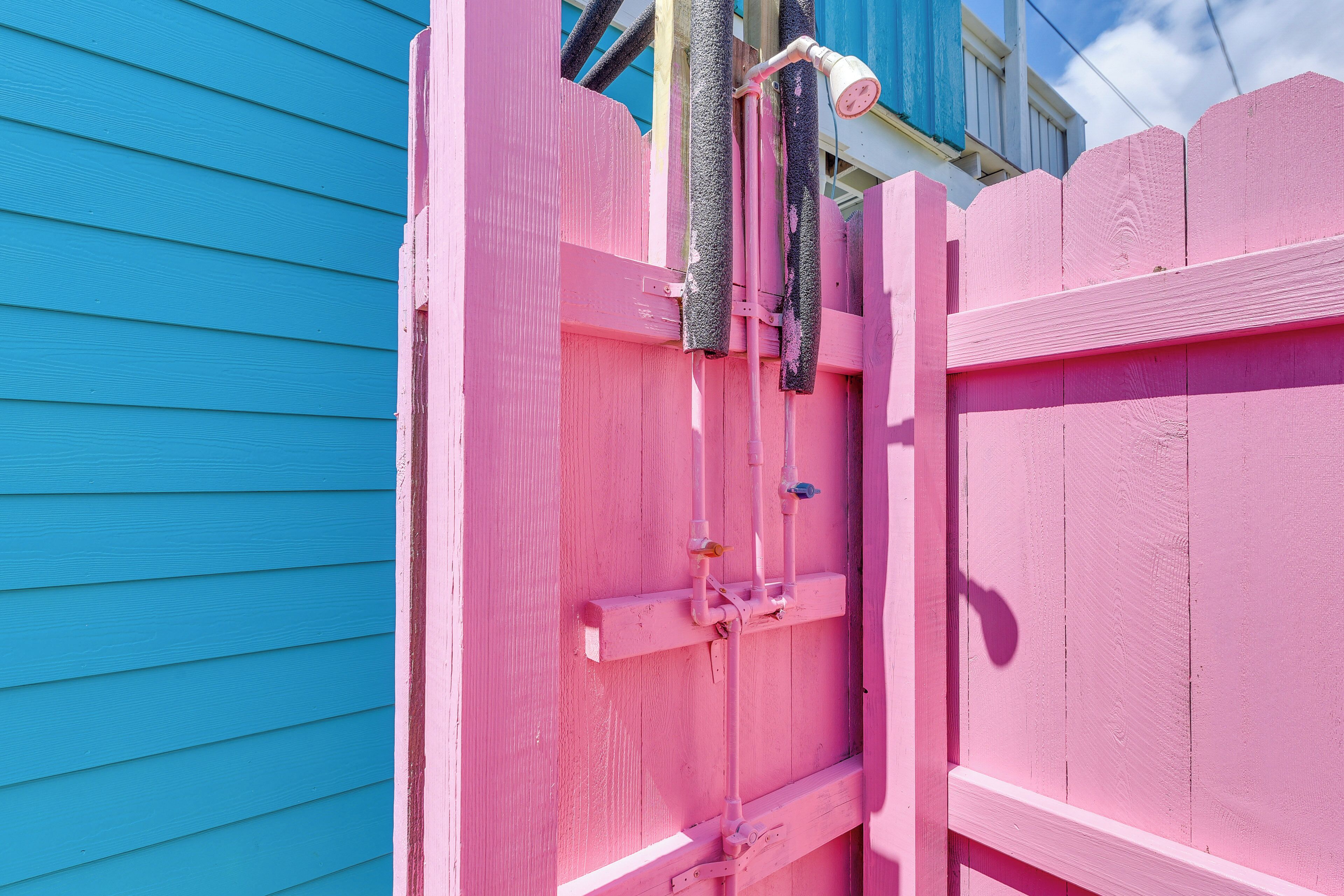 A pink wooden gate with a metal latch and a hose attached to it.