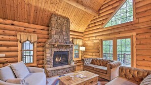 A log cabin interior with a stone fireplace, wooden furniture, and large windows. - Splendid Family Cabin w/ Hot Tub & Grill! (Lake City)
