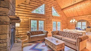 A log cabin interior with a fireplace, two sofas, a coffee table, and a dining area with a chandelier. - Splendid Family Cabin w/ Hot Tub & Grill! (Lake City)