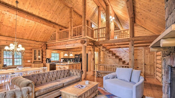 A spacious log cabin interior with a high ceiling, a dining area, a living room with a fireplace, and a staircase leading to an upper level. - Splendid Family Cabin w/ Hot Tub & Grill! (Lake City)