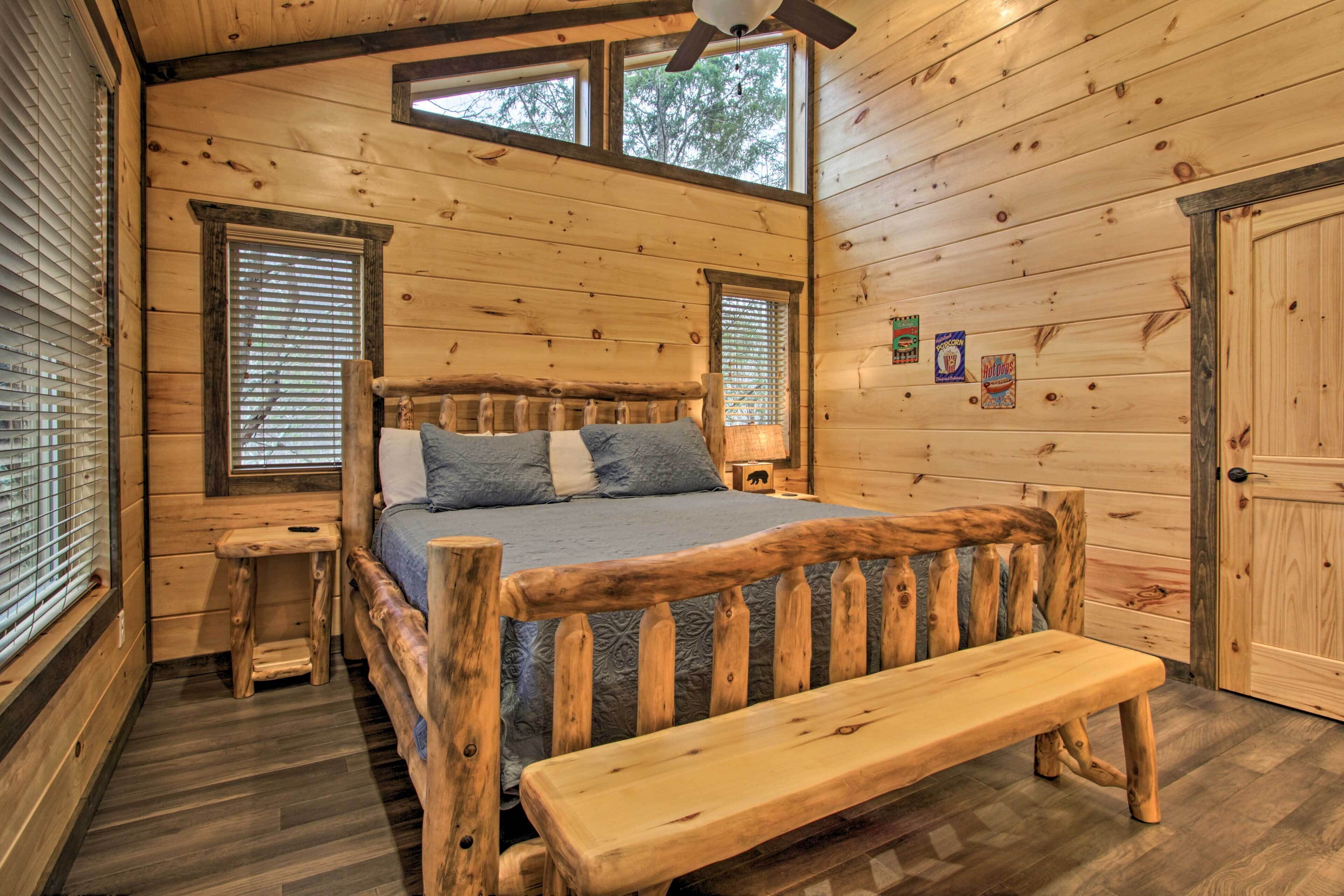 A wooden cabin bedroom with a bed, bench, and two windows.