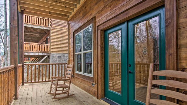 Une cabane en bois avec une véranda, une chaise berçante et une porte dotée d’un cadre vert.