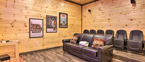 A wooden-paneled room with a sofa, chairs, and posters on the walls.