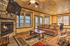 L’intérieur chaleureux d’un chalet avec une cheminée en pierre, un plafond en bois et une grande fenêtre donnant sur une terrasse.