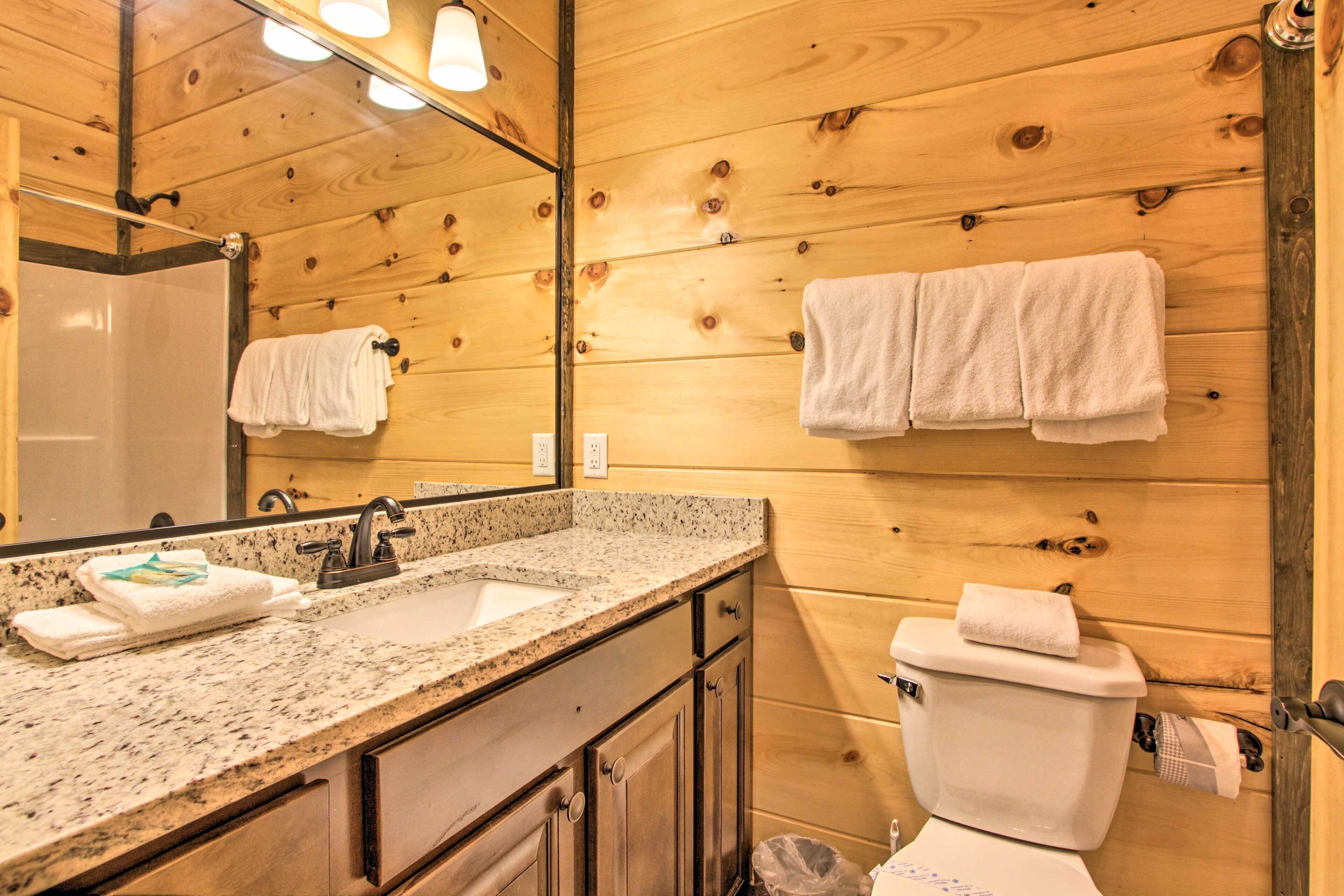 Ein Badezimmer einer Holzhütte mit einem Waschbecken aus Granit, einem Spiegel und einer Toilette, an der eine Handtuchstange angebracht ist.