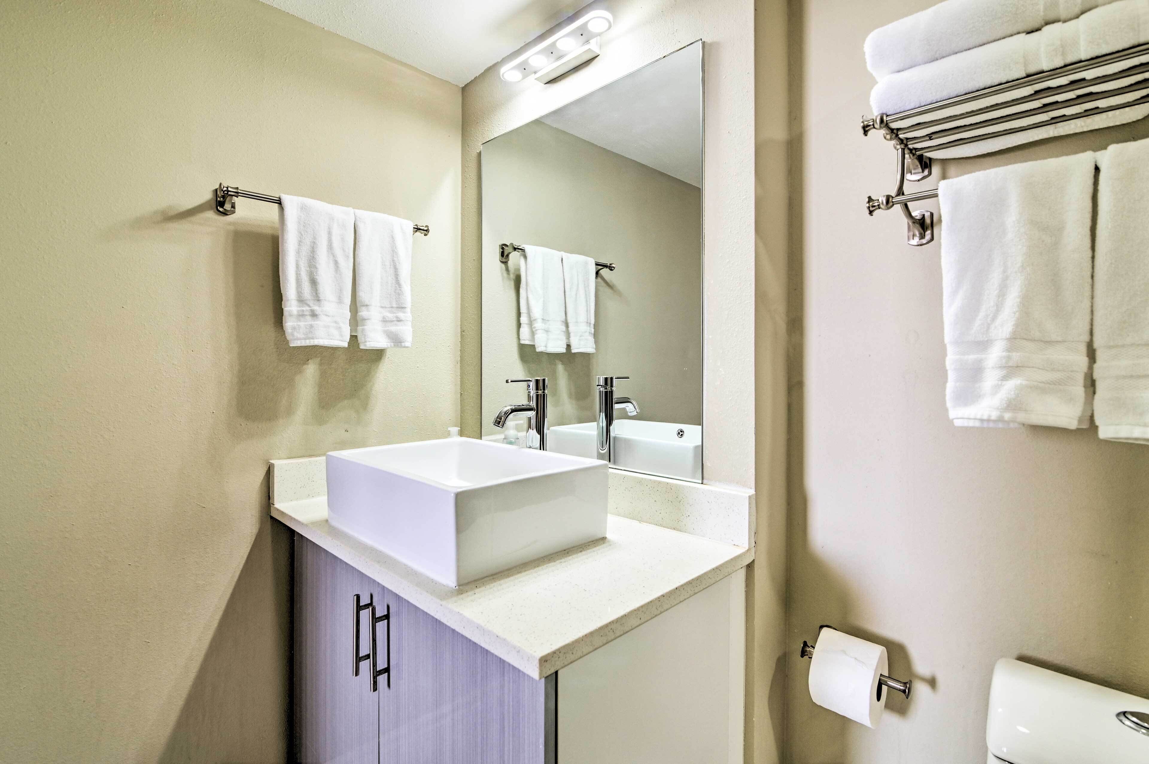 A modern bathroom with a white sink, a large mirror, and multiple towels hanging on towel racks.