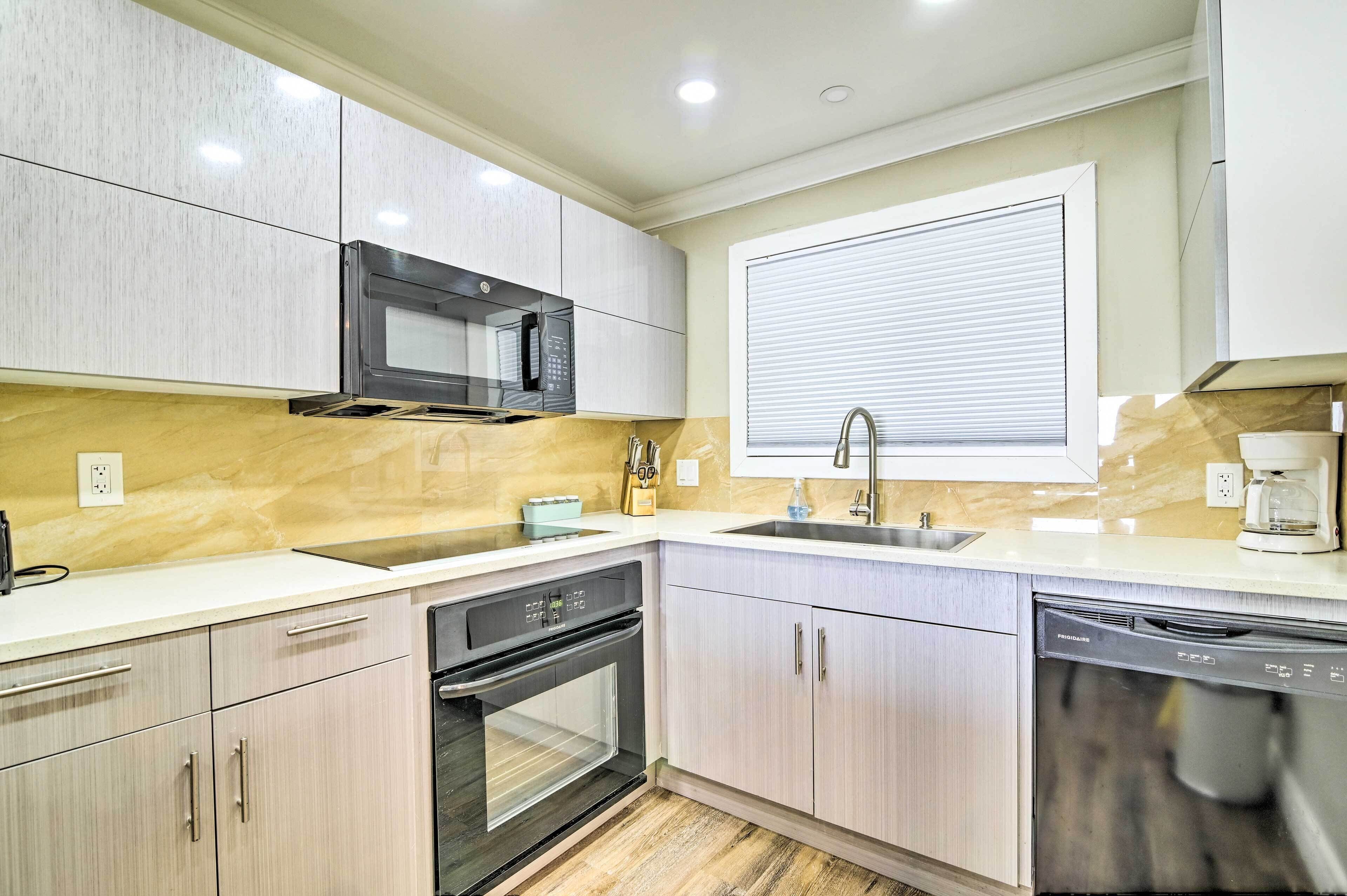 A modern kitchen with a built-in microwave, oven, and dishwasher, light-colored cabinetry, and a window with blinds.