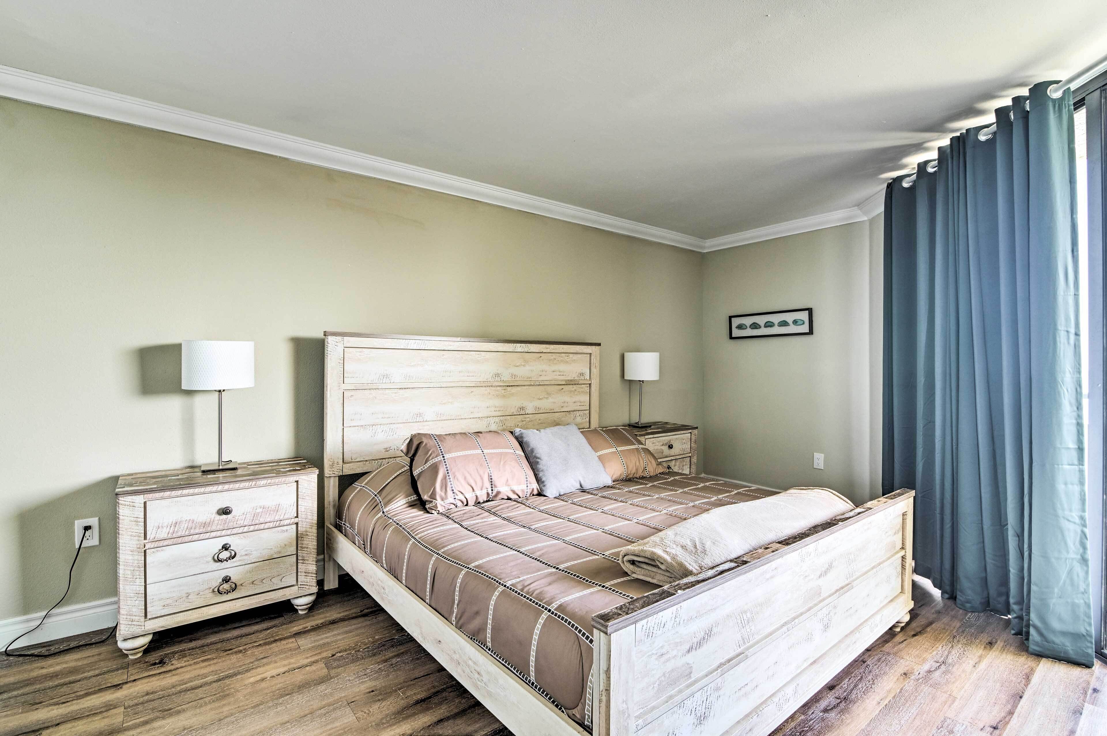 A bedroom with a wooden bed, two bedside tables, a nightstand, and a window with curtains.