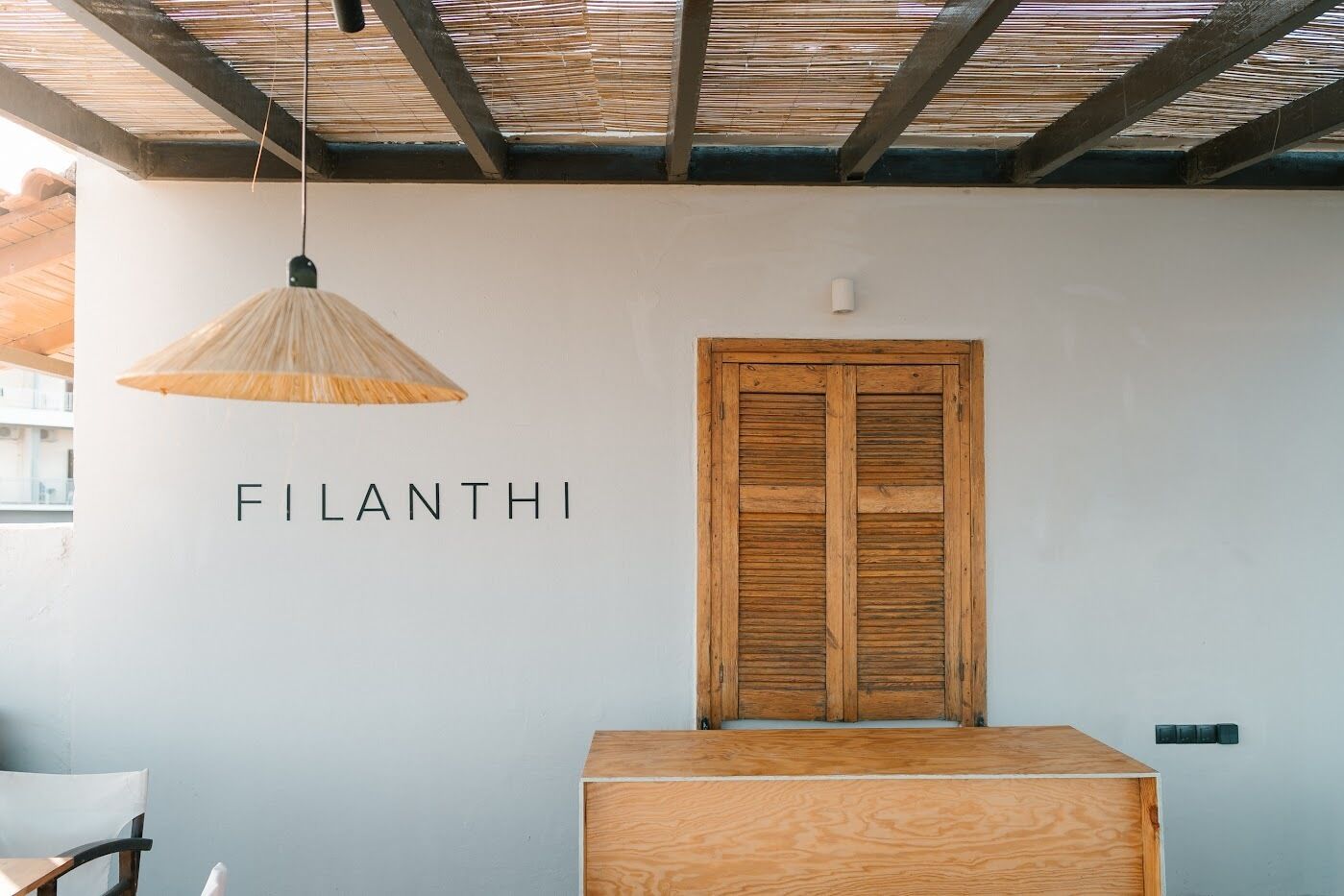 A room with a wooden door labeled "FILANTHI," a hanging light fixture, and a wooden table.