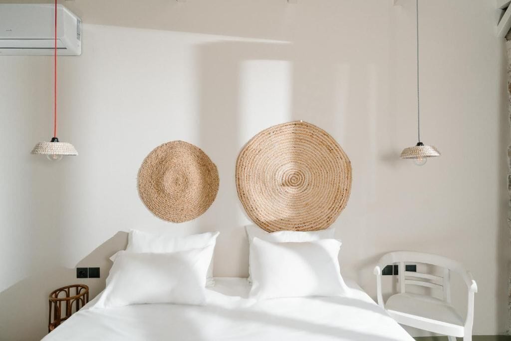 Une chambre à coucher avec un lit, des oreillers blancs, deux décorations murales en tissu, une chaise blanche et un luminaire suspendu.