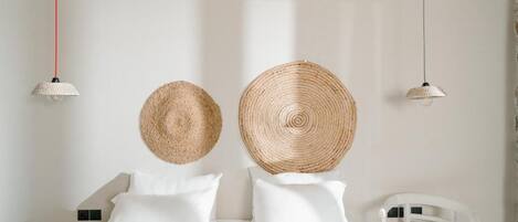 Une chambre à coucher avec un lit, des oreillers blancs, deux décorations murales en tissu, une chaise blanche et un luminaire suspendu.
