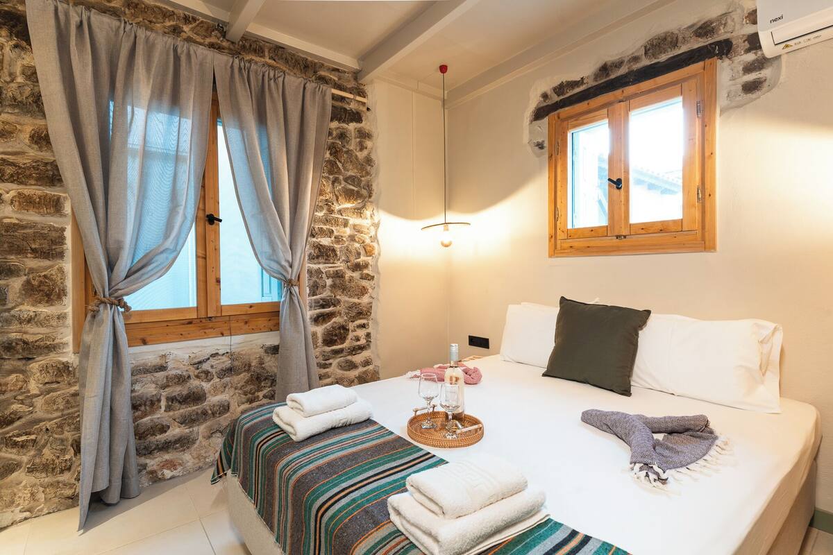 A cozy room with a stone wall, a bed with white linens, a wooden window, and a hanging light fixture.