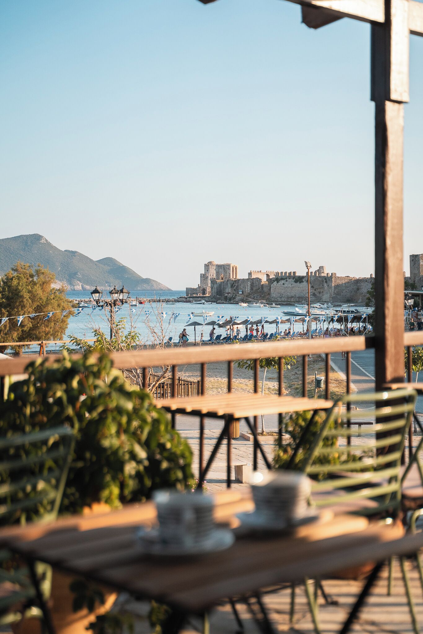 A seaside restaurant with outdoor seating overlooking the sea and a historic building in the background.