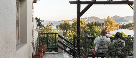Una terraza con suelo de piedra, plantas en macetas y vistas a montañas y una masa de agua.