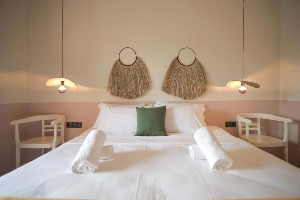 A neatly made bed with white linens, a green pillow, and two white chairs.