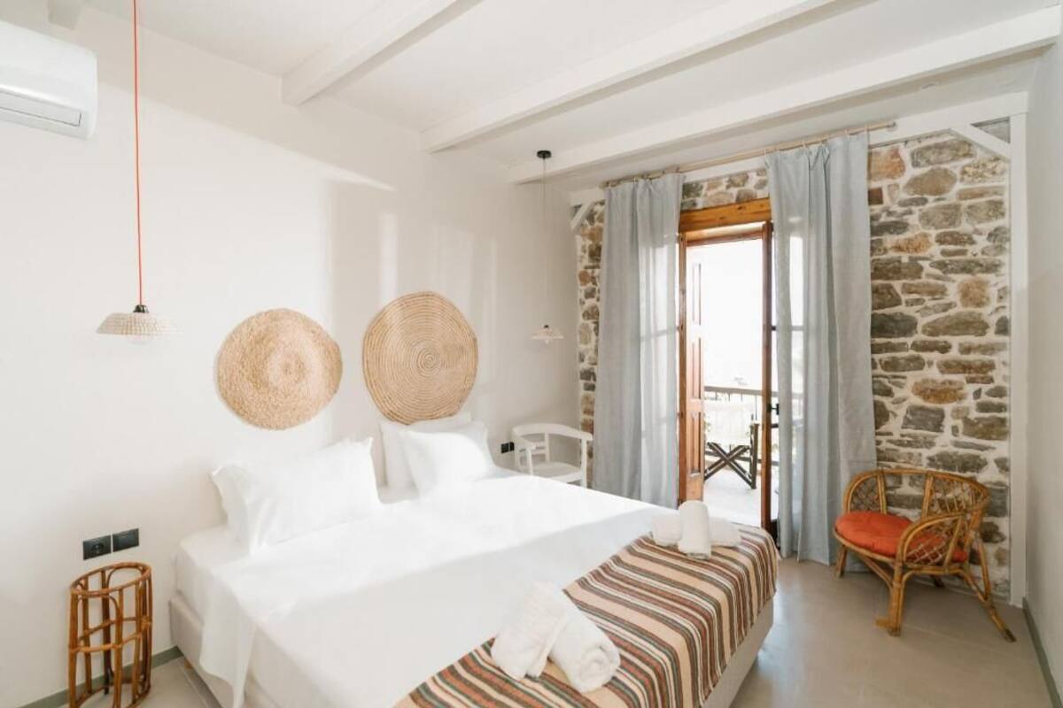 A bedroom with a bed, a wicker chair, and a stone wall.