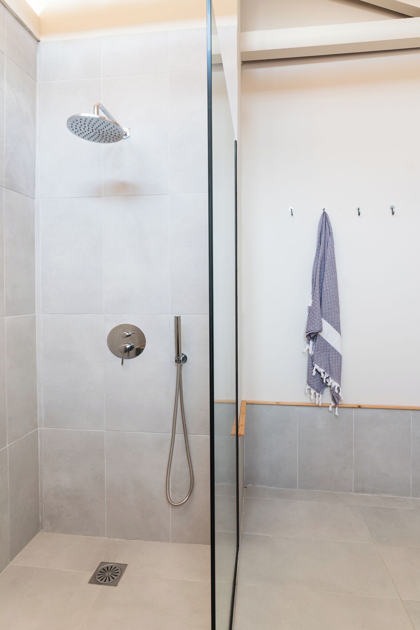 A shower area with a glass door, a handheld showerhead, and a towel rack with a towel.