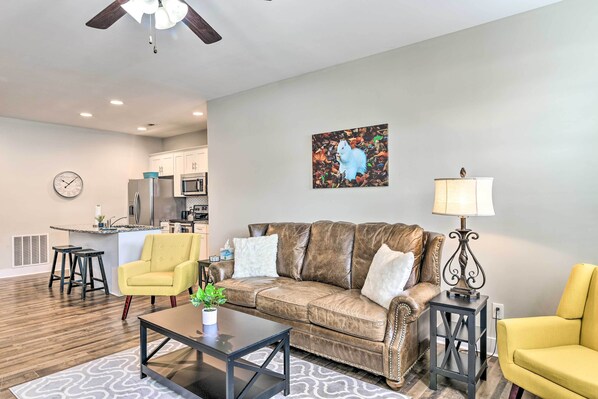 A living room with a brown leather sofa, yellow armchairs, a coffee table, and a kitchen in the background. - Bowling Green Apartment in the Heart of Town! (Bowling Green)