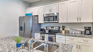 A modern kitchen with white cabinets, stainless steel appliances, a granite countertop, and a potted plant. - Bowling Green Apartment in the Heart of Town! (Bowling Green)