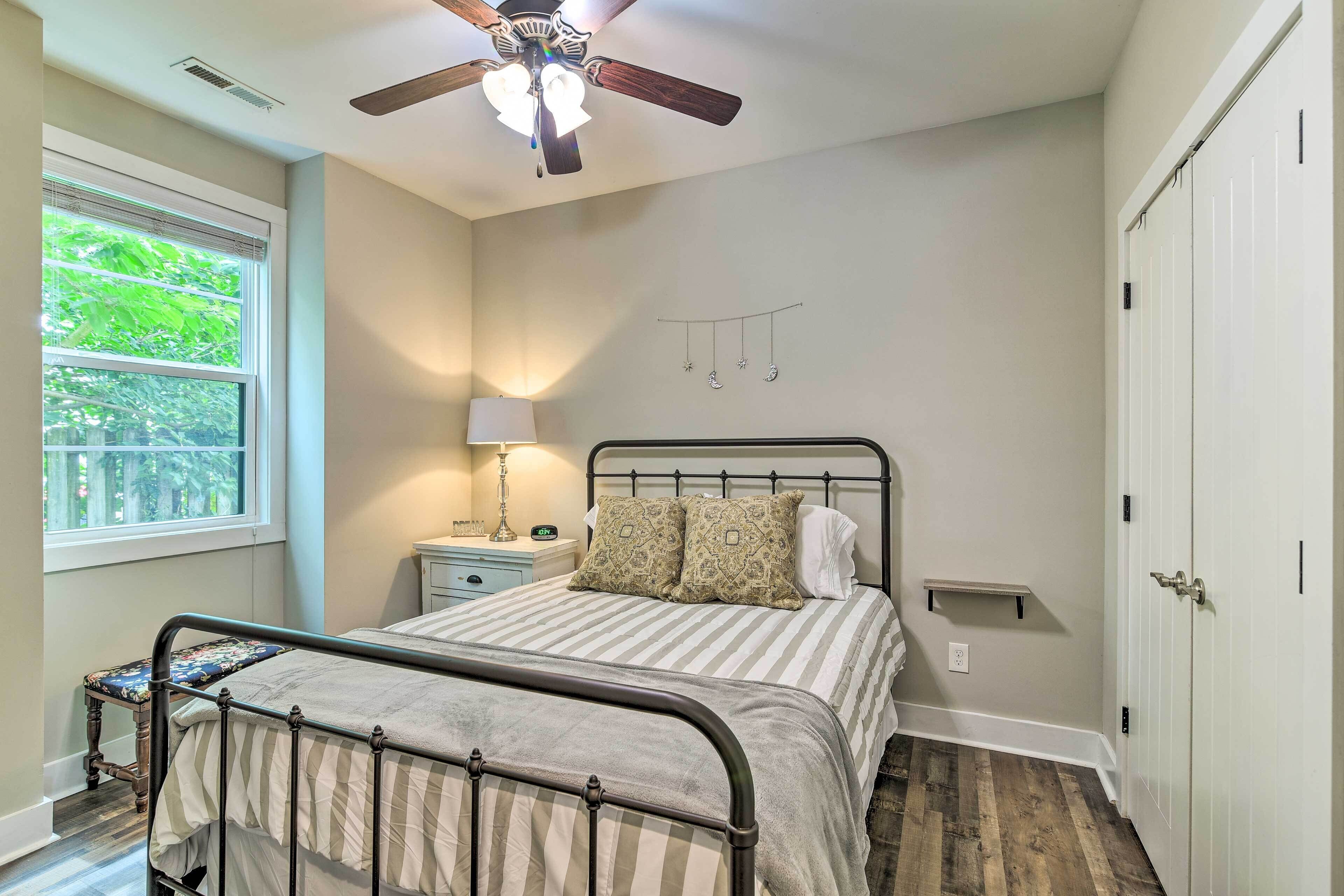 A bedroom with a bed, a nightstand, a lamp, a ceiling fan, a window, and a door.