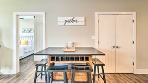 A dining area with a table and chairs, a 'gather' sign on the wall, and a door to the right. - Bowling Green Apartment in the Heart of Town! (Bowling Green)