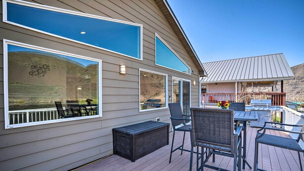 A deck with outdoor furniture, large windows, and a view of a hilly landscape.