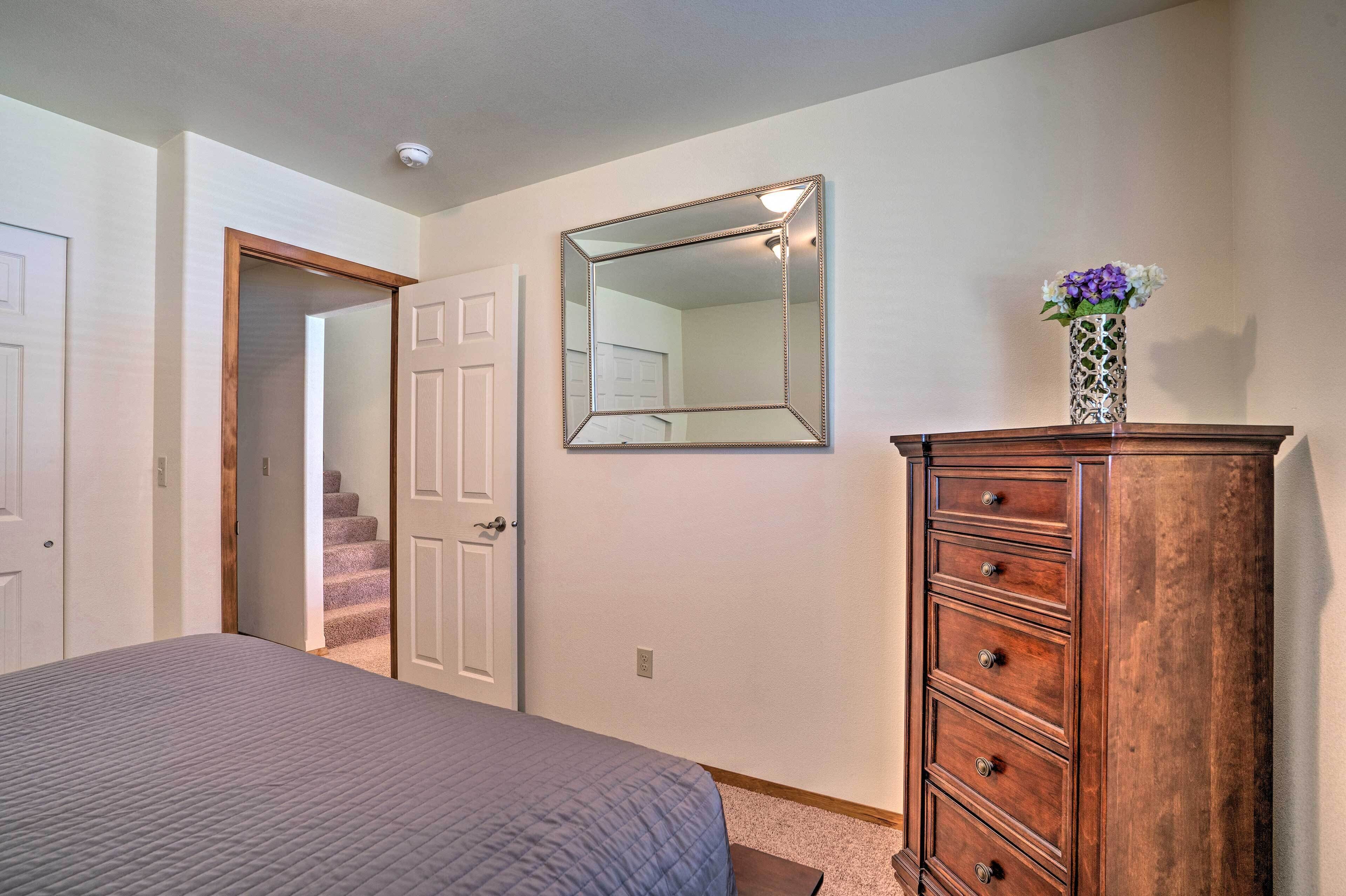 A bedroom with a bed, a dresser, a mirror, and a door leading to a staircase.