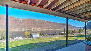 A covered outdoor area with a view of a mountainous landscape, a grassy field, and a few buildings in the distance.