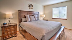 A bedroom with a large bed, two bedside tables, a nightstand, a wall clock, and a window with blinds.
