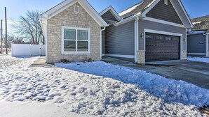 Une maison à deux étages avec une façade en pierre, un garage et une allée recouverte de neige.