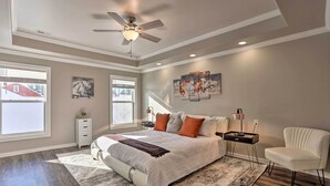 Une chambre à coucher avec un grand lit, un ventilateur de plafond, une table de chevet, une chaise et des œuvres d’art accrochées aux murs.