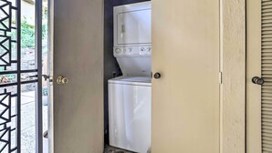 A laundry room with a washing machine and dryer, a door with a metal gate, and a concrete floor. - Mtn-view Balcony + Pool Access: Palm Springs Gem (Palm Springs)