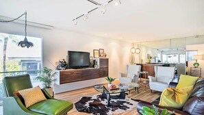 A modern living room with a green armchair, a leather sofa, a glass coffee table, and a large window. - Mtn-view Balcony + Pool Access: Palm Springs Gem (Palm Springs)