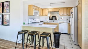 A modern kitchen with wooden cabinets, a white countertop, and a central island with stools. - Mtn-view Balcony + Pool Access: Palm Springs Gem (Palm Springs)
