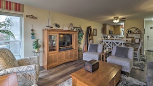 Ein Wohnzimmer mit einem Holzschrank, zwei grauen Sofas, einem Couchtisch und einem Essbereich mit weißem Tisch und Stühlen.